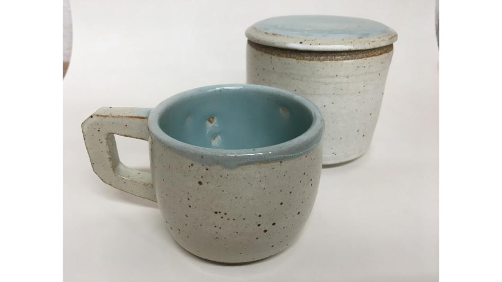 Speckled mug with handle with a lidded jug behind it.