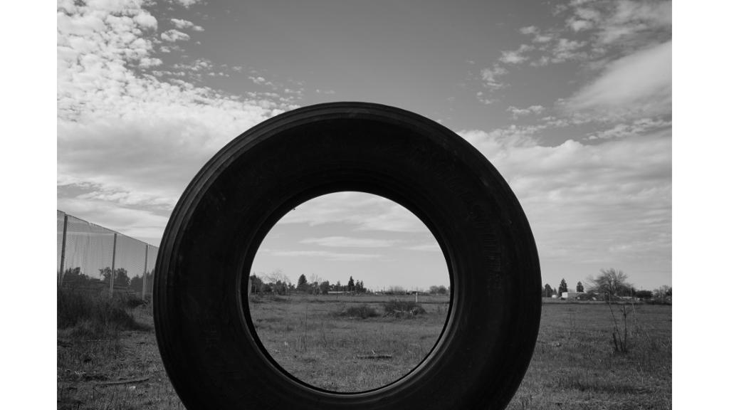 Black and white photo of a tire and empty field