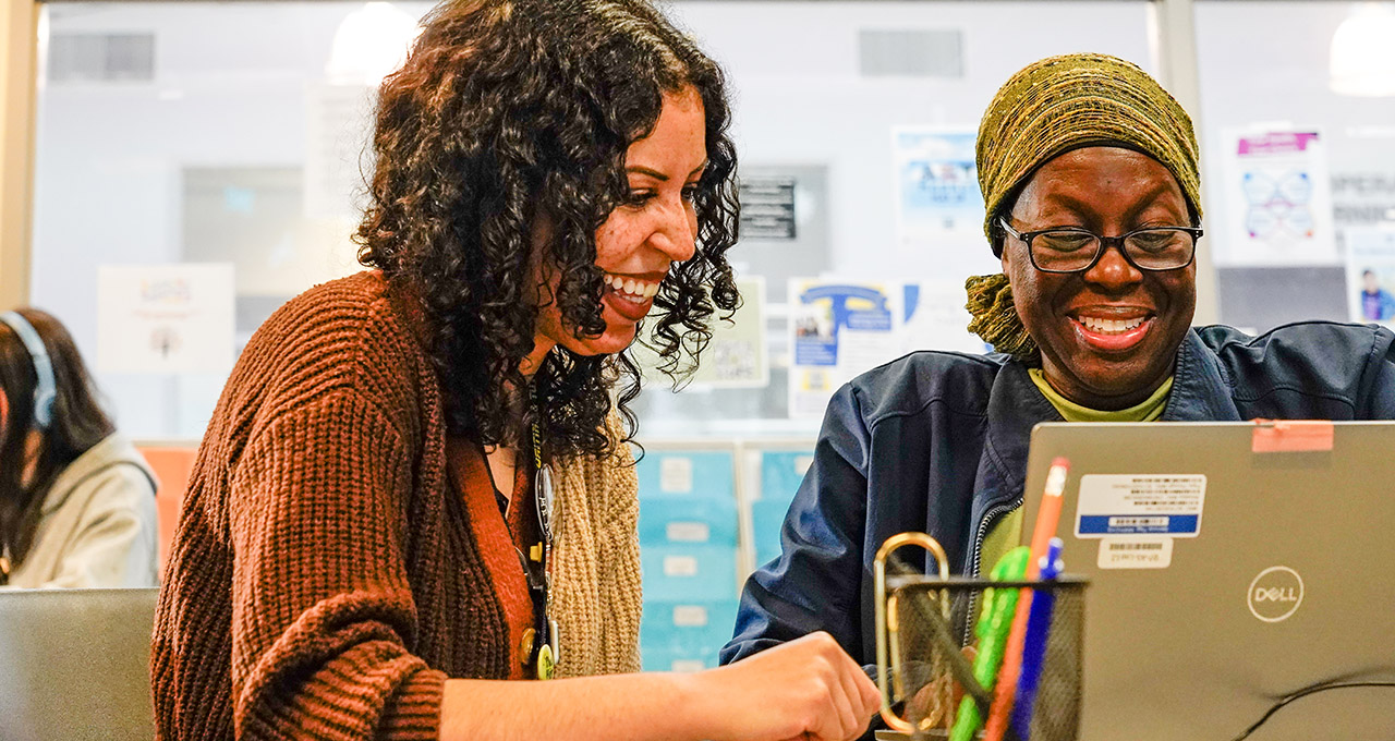 Two women smiling working on a laptop in the TCC Writing & Tutoring Center 