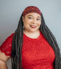 A headshot of Jasmine Iona Brown wearing a red headband and red dress