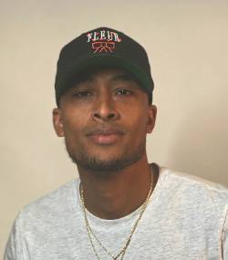 A headshot of Lourdes wearing a baseball cap and a white t-shirt