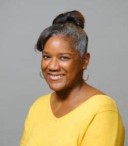 a headshot of an artist wearing yellow on a gray background