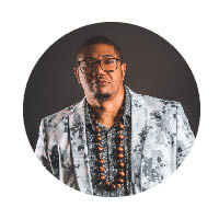 artist in a white suit jacket with beads around neck