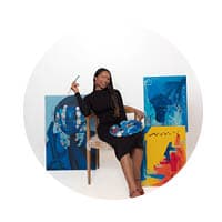 female sitting with paint brush in hand and art behind her.