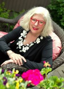 Photo of instructor Josie Emmons Turner sitting in a patio chair with statement-red glasses frames and a big smile.