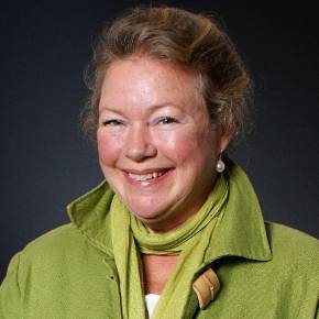 Denise Frisino with hair hair pulled back, wearing a green jacket and scarf, and pearl earrings; dark background
