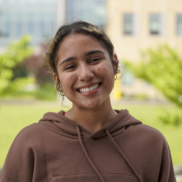 woman with curly hair pulled back in a tan hoody smling