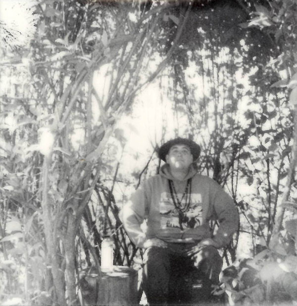 Black and white photo of Kalvin "Wovoka" Satiacum sitting in a forest. 