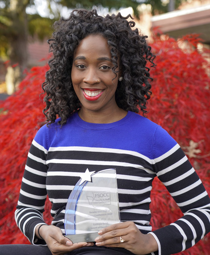 Latoya reid with an award in front of a tree near building F1