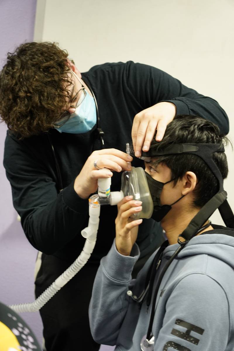 A student places a breathing mask on his peer