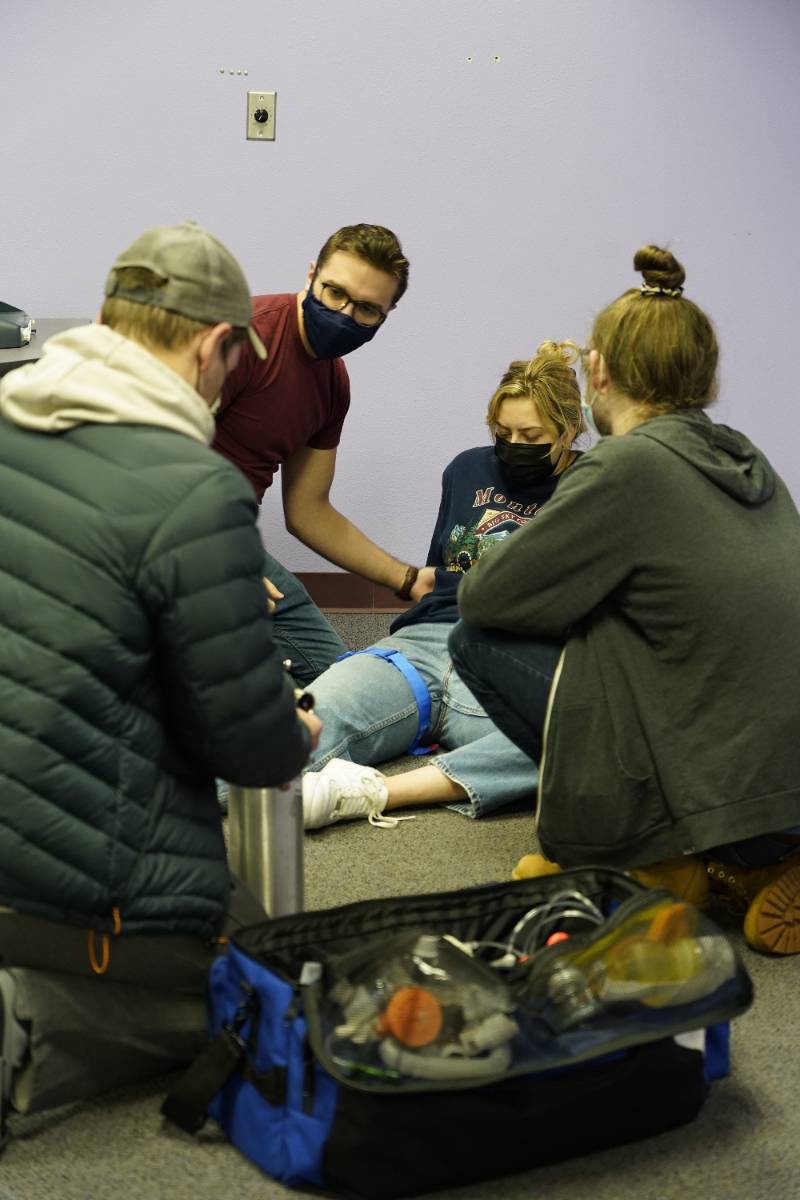 A cluster of EMT students are bandaging a peer's leg