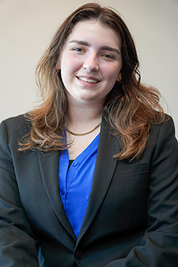 Image of a woman with brown hair wearing a blue shirt and a black jacket. 