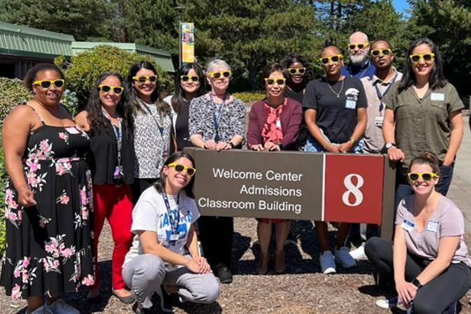 a large group of people in sunglasses standing around TCC's Building 8 Welcome Center sign 
