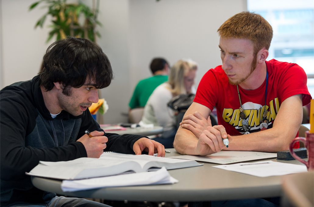 A student and a tutor sit at a table discussing chemistry.