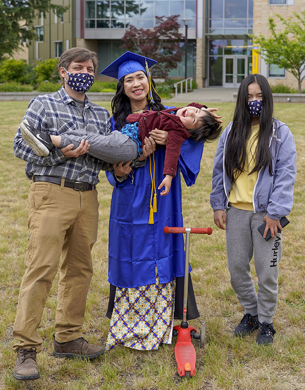 woman in commencement regalia with man and two kids