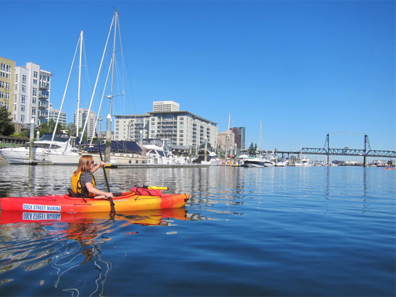 A woman in a red kayak paddling towards the Murray Morgan Bridge.